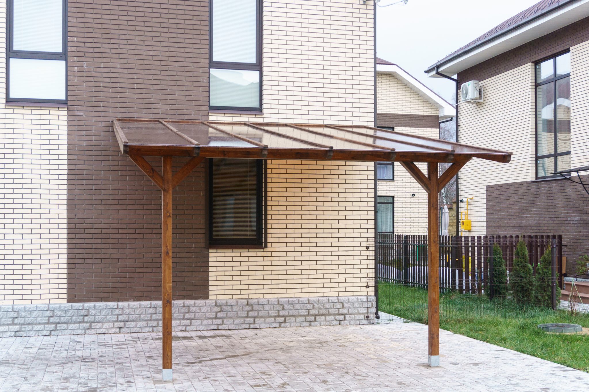 Wooden carport with a transparent roof made of tinted plastic.